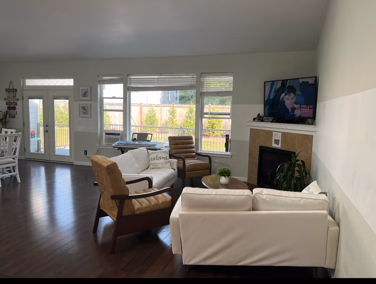 Bright living room with white sofas, brown chairs, fireplace, and wall-mounted TV.