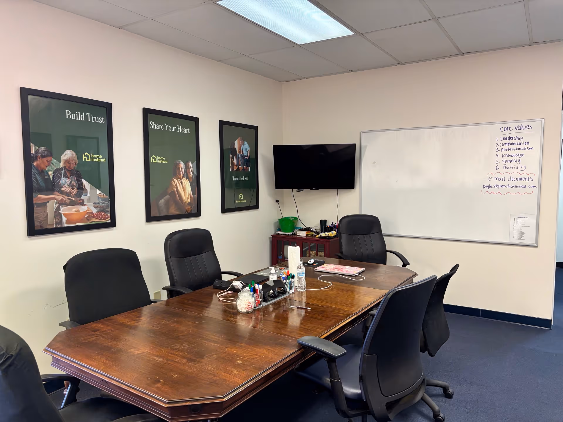 A conference room with a wooden table, chairs, posters, a TV, and a whiteboard.