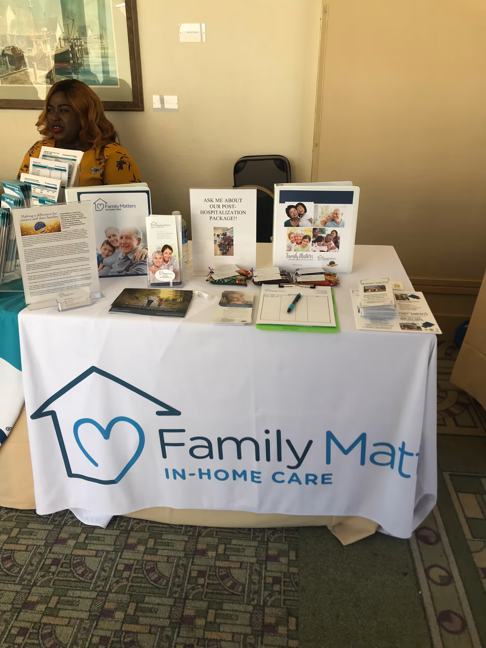 Indoor booth table with Family Matters In-Home Care brochures and a staff member.