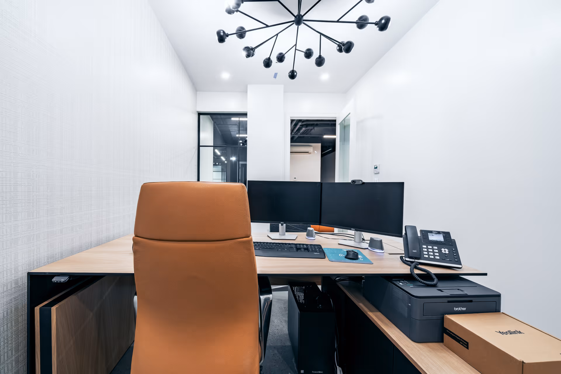 Modern office workspace with dual monitors, a brown chair, keyboard, phone, and printer.