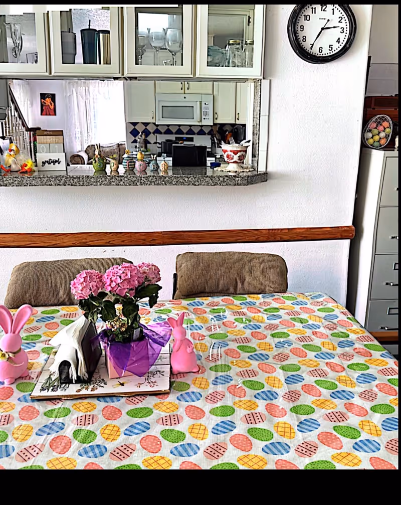 Cozy kitchen and dining area with colorful Easter tablecloth, flowers, decorative bunnies, and a wall clock.