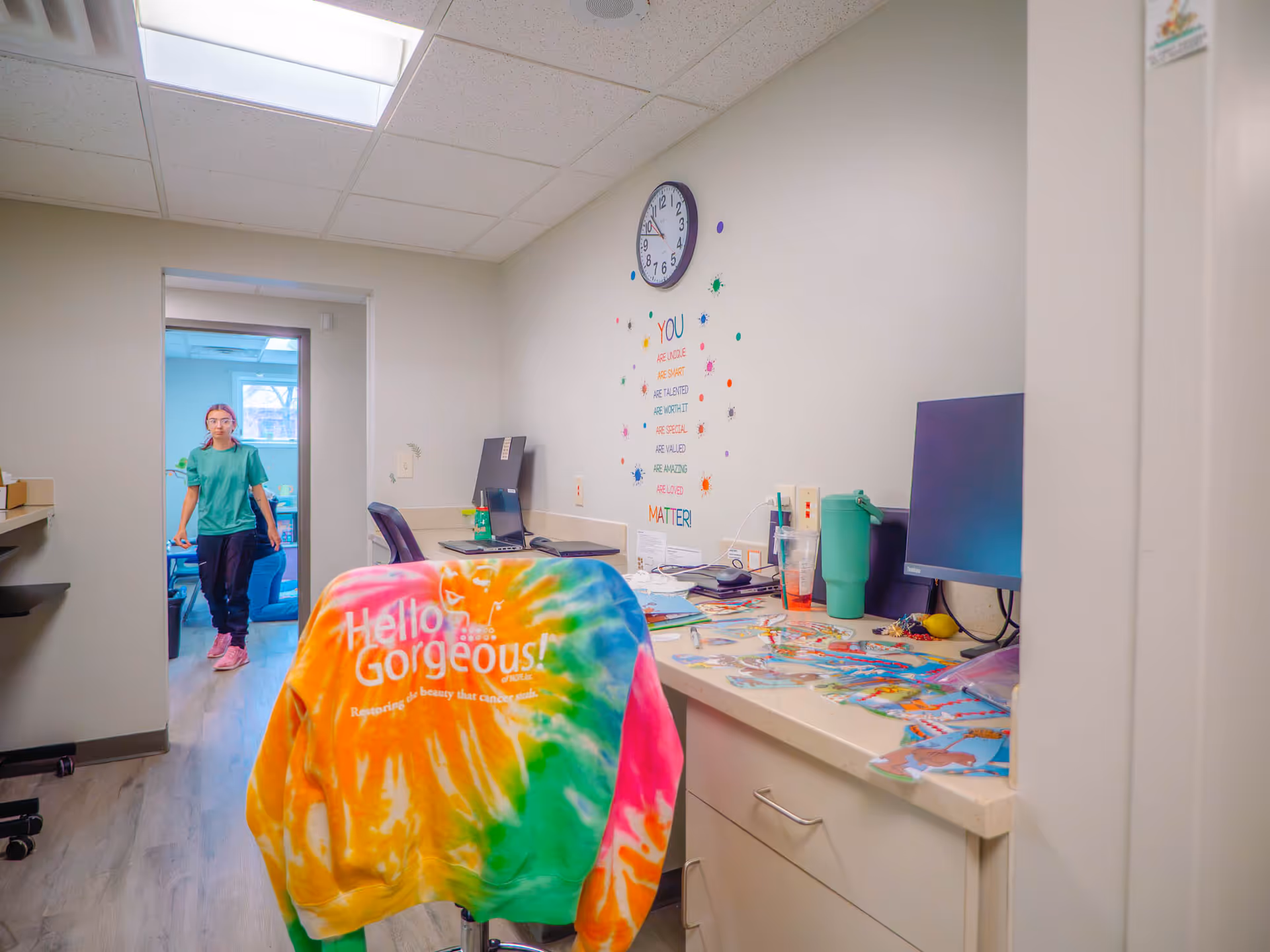 Clinical office space with a desk, computer, and a staff member in scrubs near a doorway.
