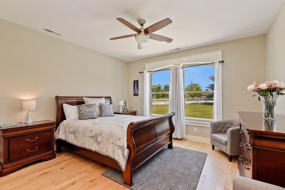 Wooden bed with matching dressers and a large window in a tidy bedroom.