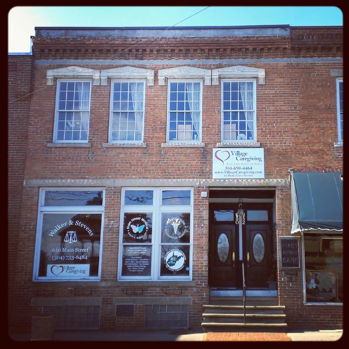 Brick two-story building with Village Caregiving sign and dark entry doors.