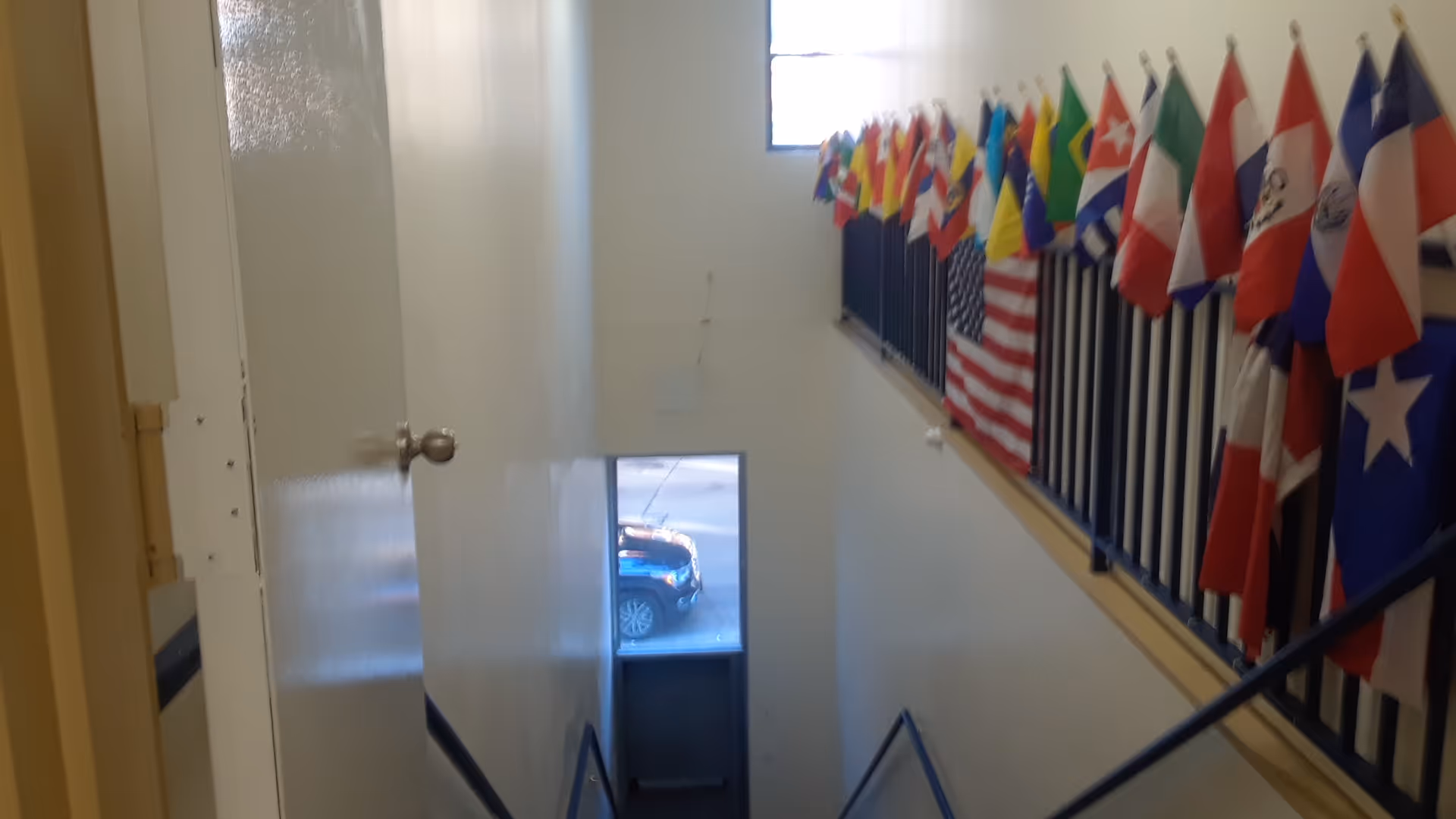 Interior stairwell with a railing lined by many international flags along the wall.