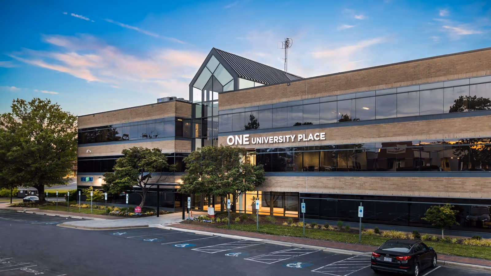 Modern brick building with glass facade labeled One University Place and parking.