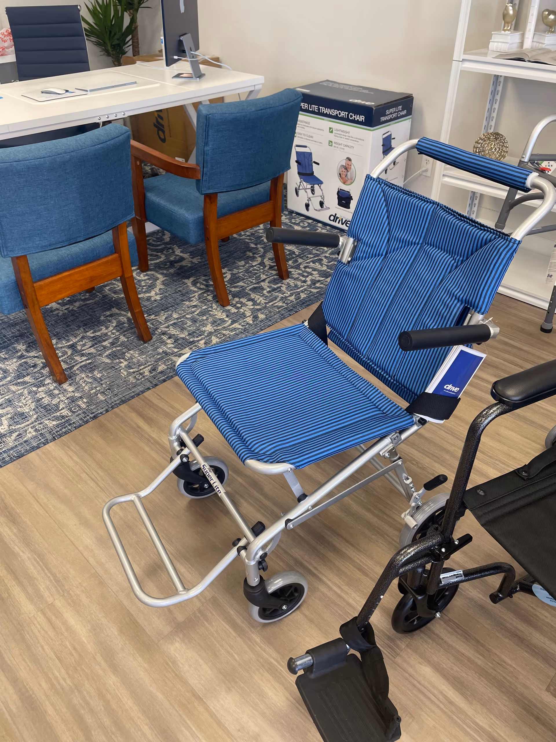 Blue striped transport wheelchair displayed in an interior showroom with a desk and chairs.
