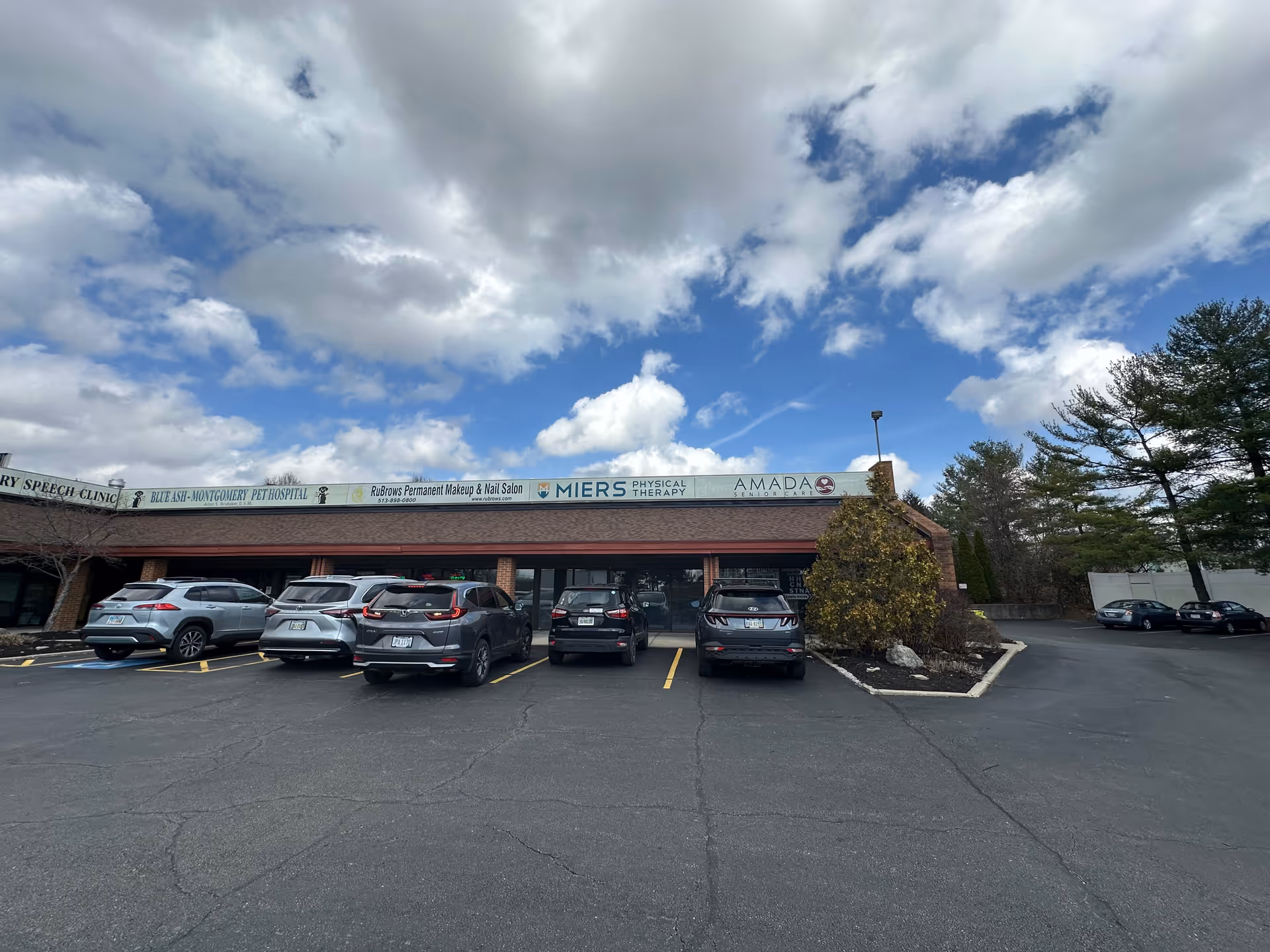 Front view of a strip mall with Amada Senior Care sign and parked cars.