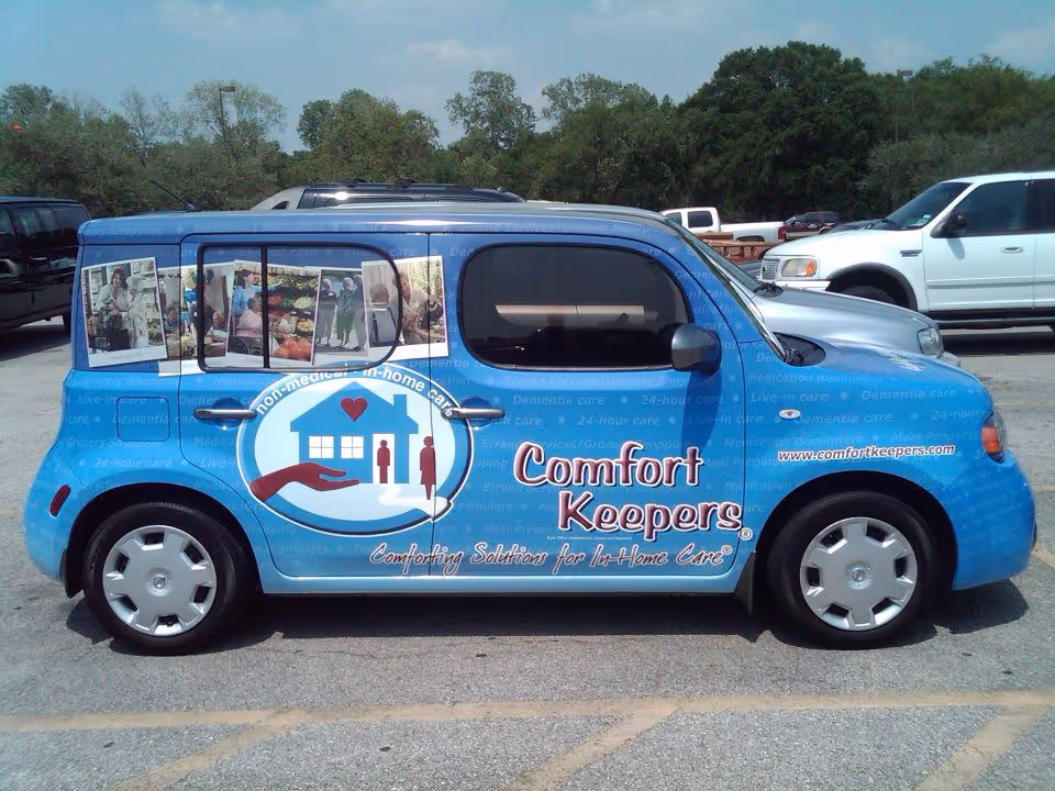 Blue Comfort Keepers van with logo and photo panels parked in a lot.