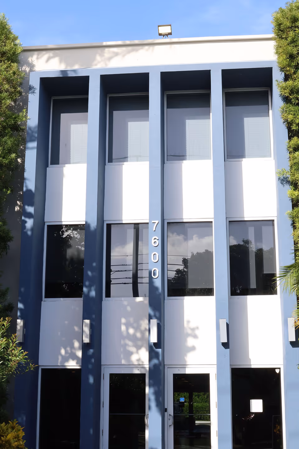 Blue modern building facade with three tall windows and an entrance at 7600.