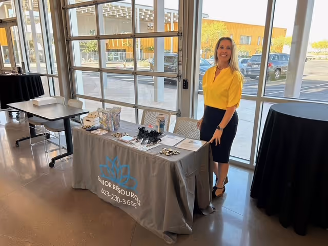 Woman in yellow blouse stands beside a promotional table in a bright interior.
