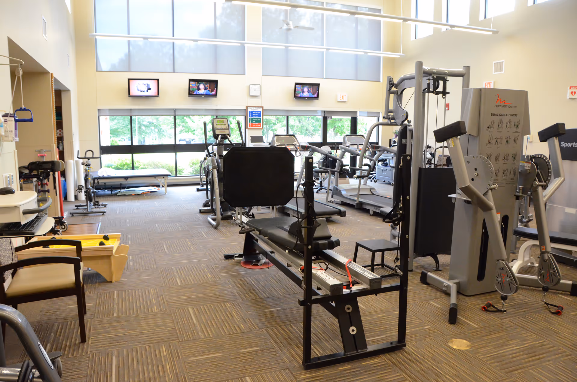 Bright gym inside a senior living facility with cardio machines, weights, and large windows.