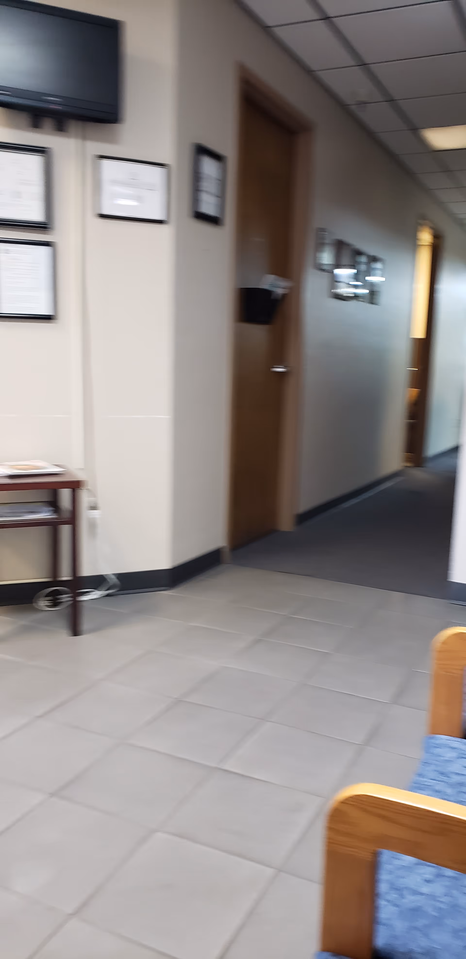 Indoor hallway in a senior living facility with framed certificates and a small table.