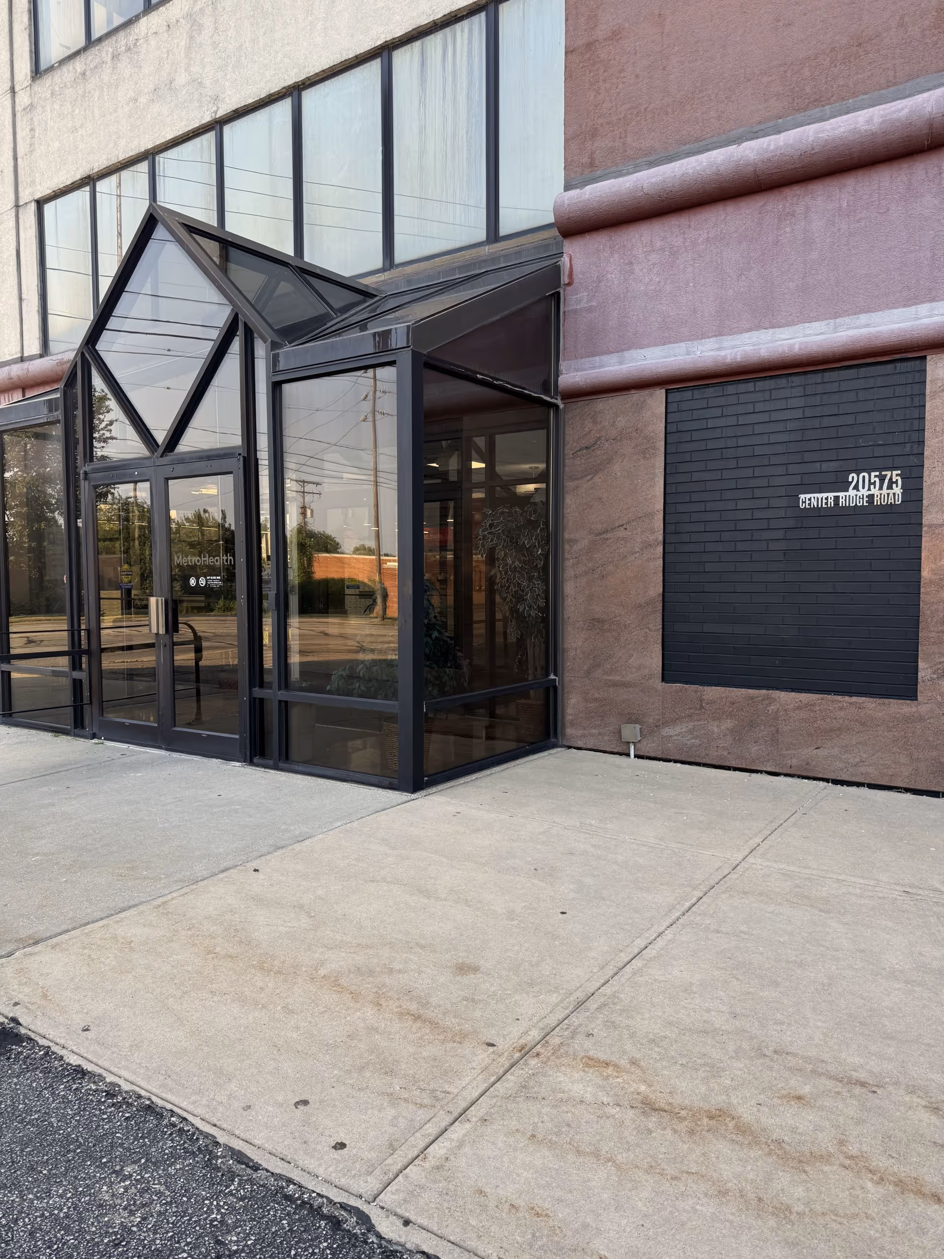 Exterior view of a building entrance with glass doors and a wall-mounted sign.