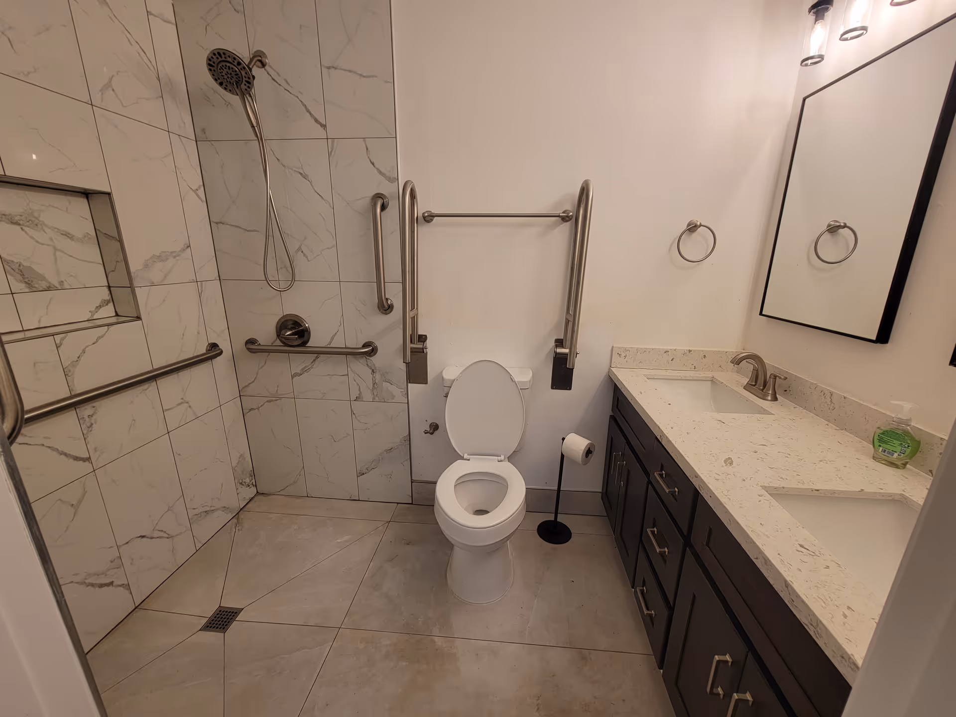 Accessible bathroom with shower, toilet, sink, grab bars, and marble-tile walls.