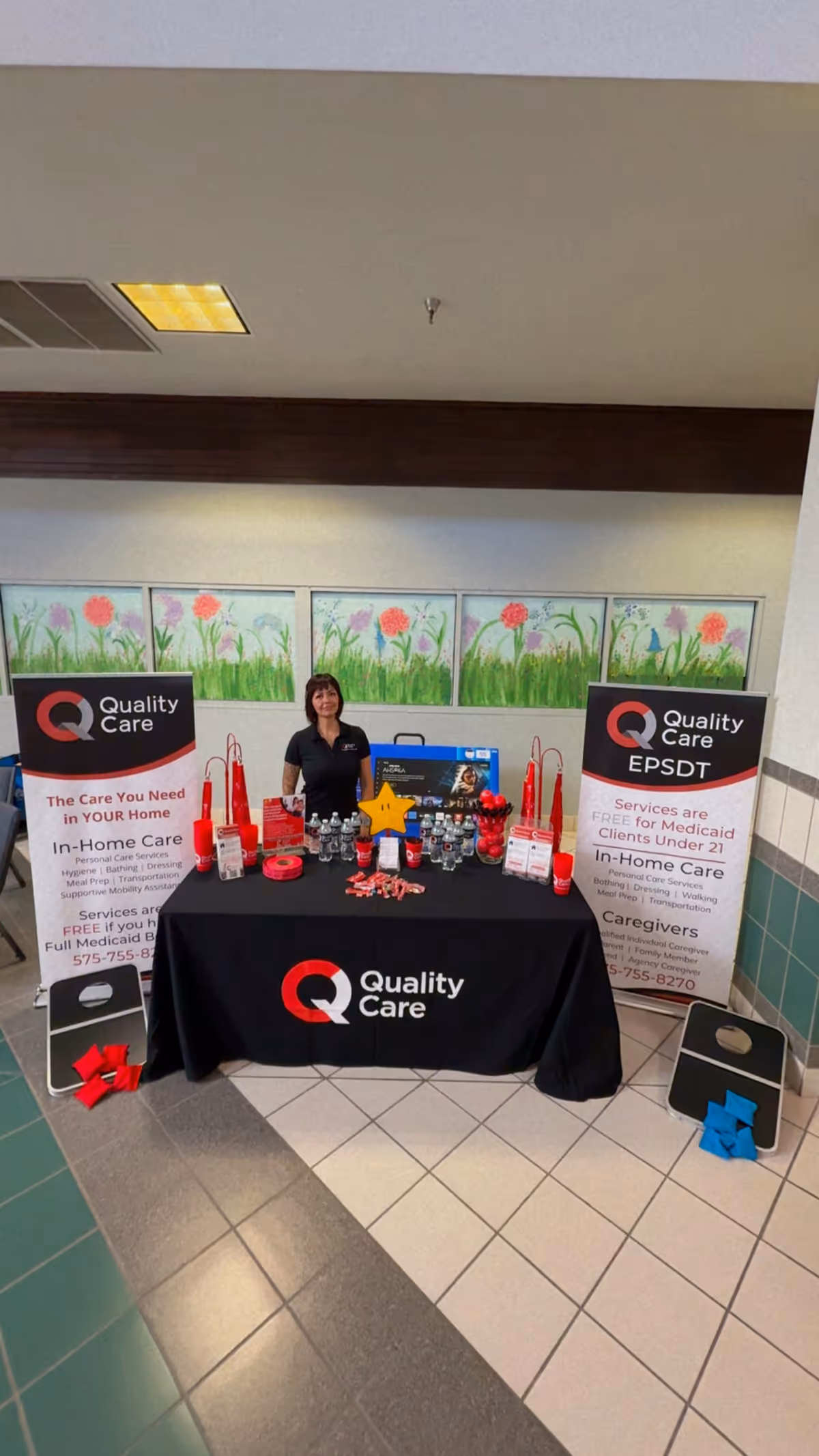 A Quality Care promotional booth with a staff member and materials in a hallway.