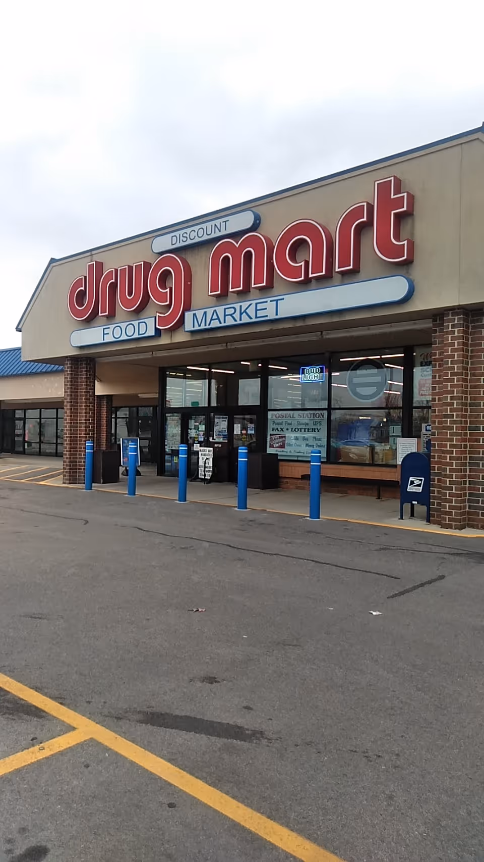 Front of a Discount Drug Mart store with a large red sign and blue parking bollards.
