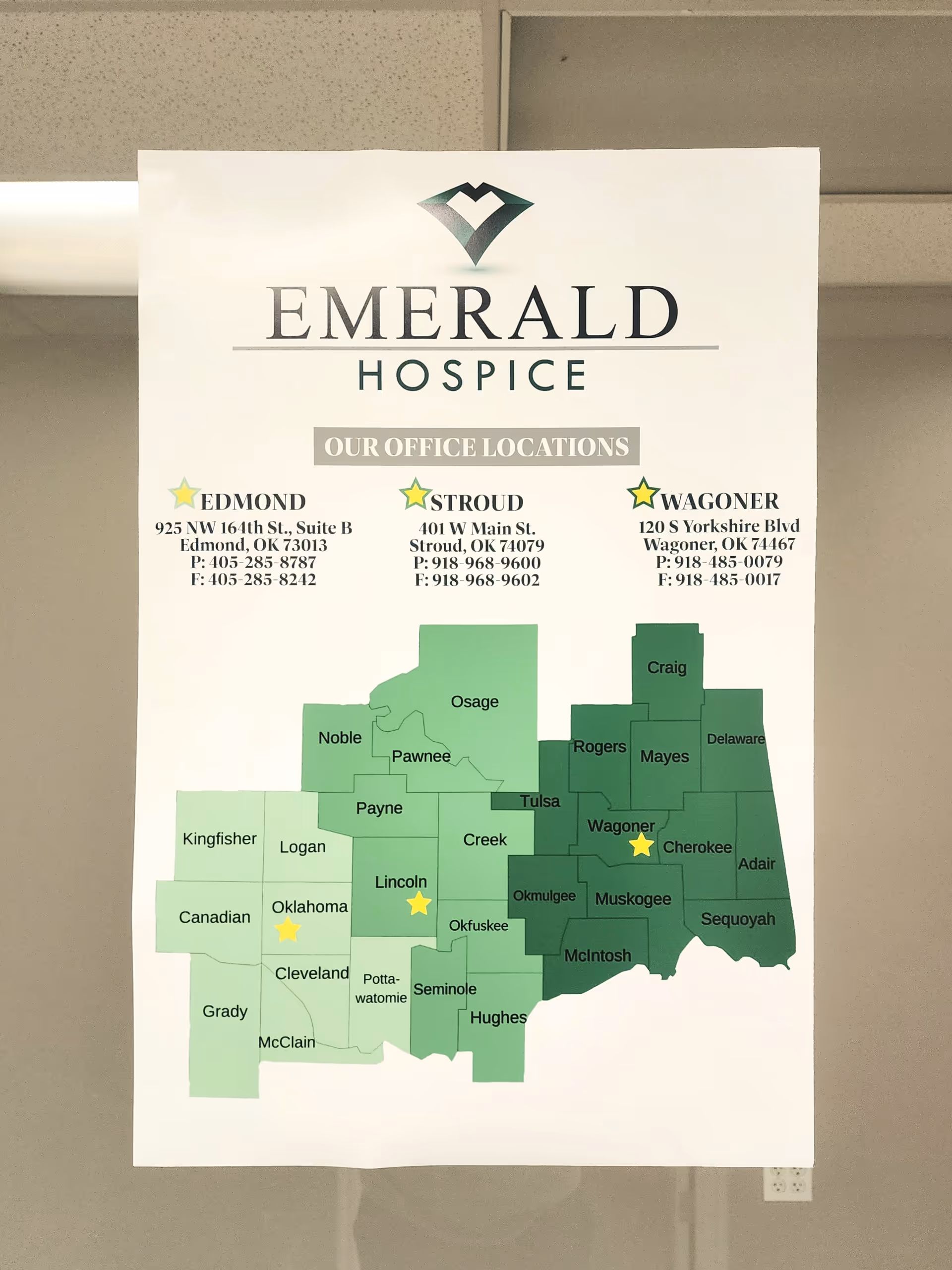A large Emerald Hospice office poster with a green Oklahoma map and contact details.