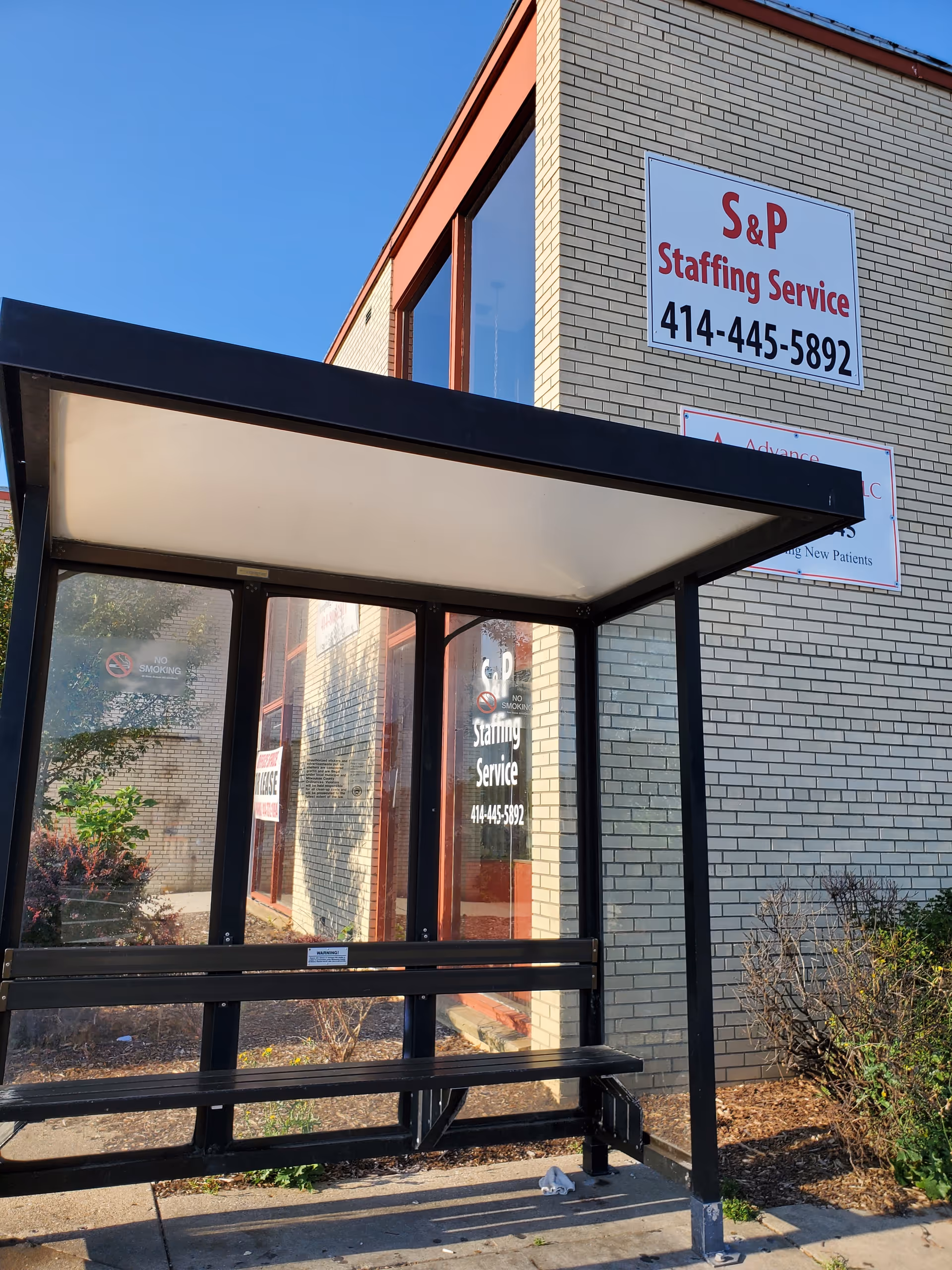 Exterior view of a brick building entrance with a glass-walled shelter and signage.