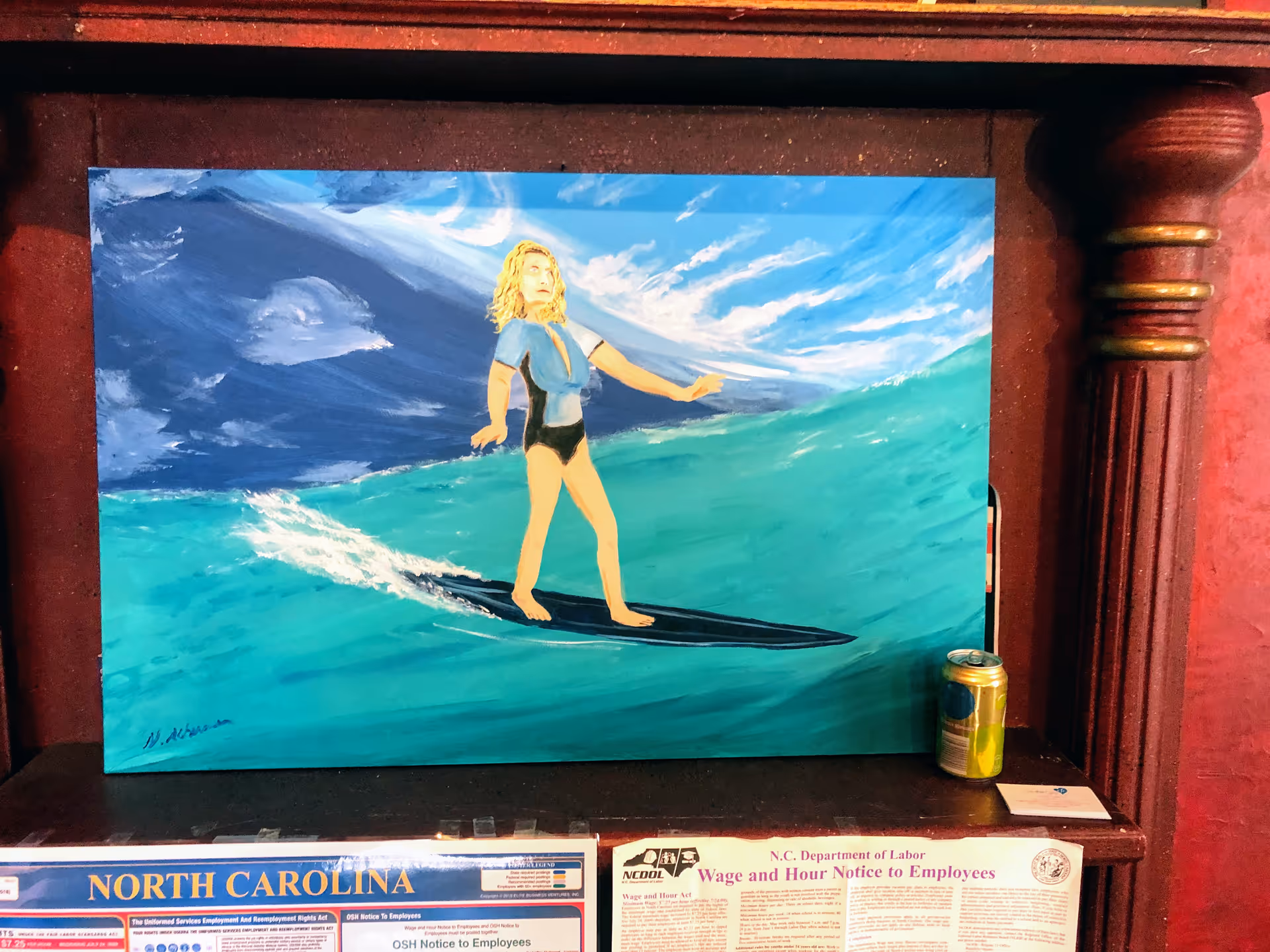 A surfing painting leans against a wall on a dark wooden shelf, with a can nearby.