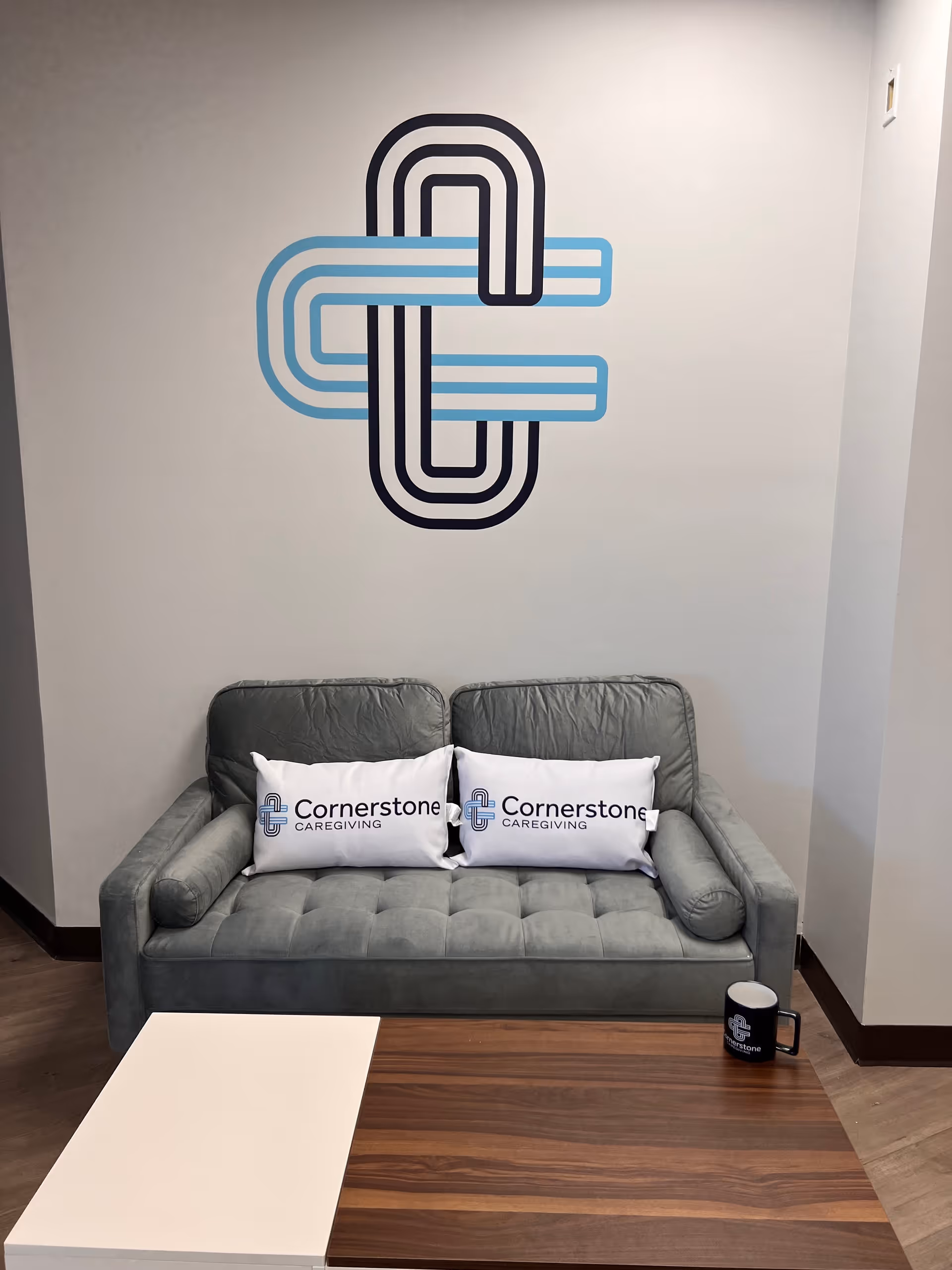 Grey sofa with Cornerstone Caregiving pillows in front of a wall logo mural.