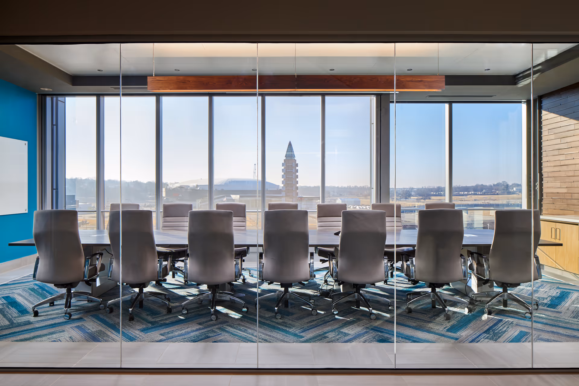 Glass-walled conference room with a long table and chairs, overlooking a cityscape.