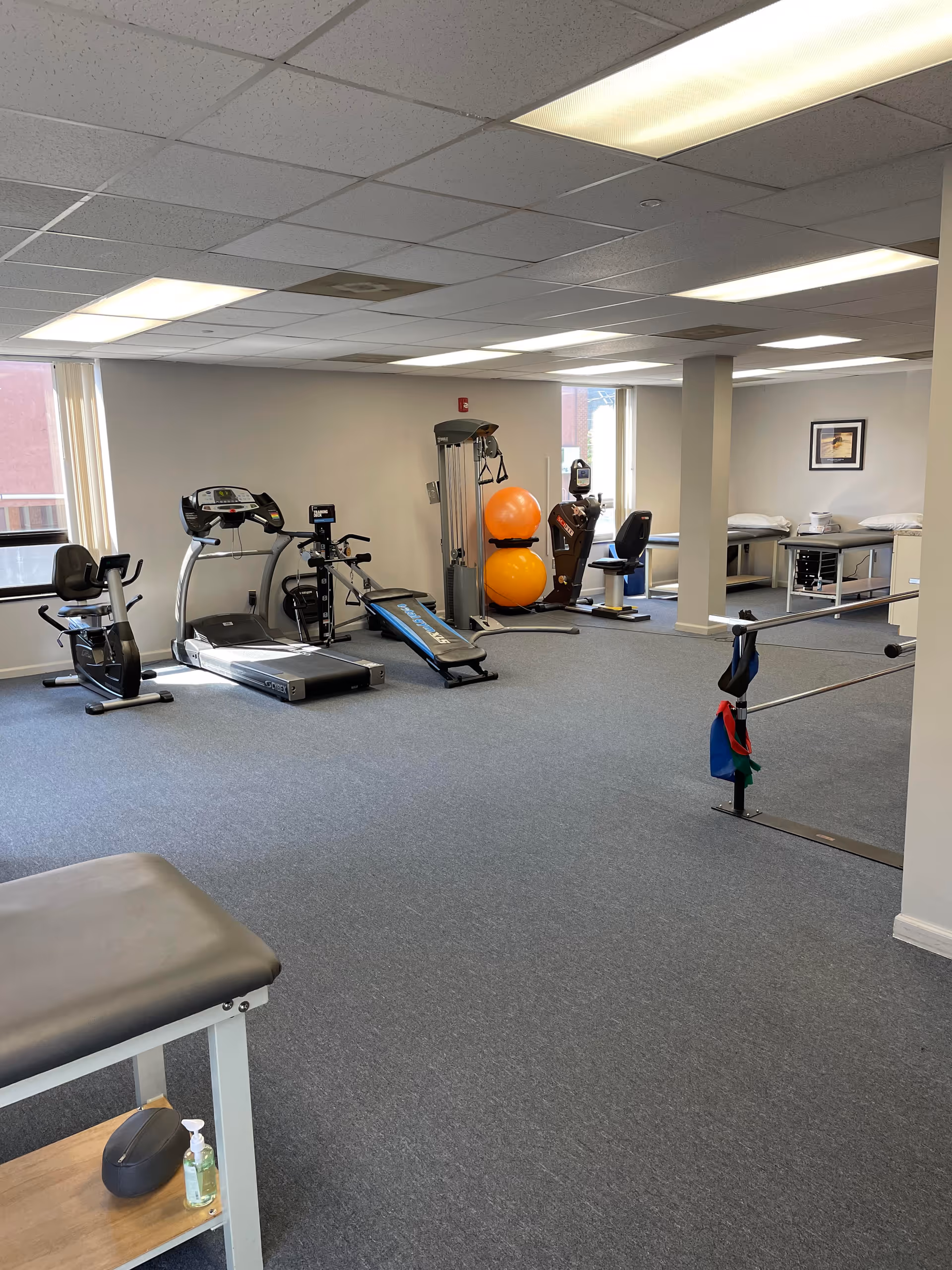 Interior therapy gym with treadmills, bikes, weights, and orange stability balls.