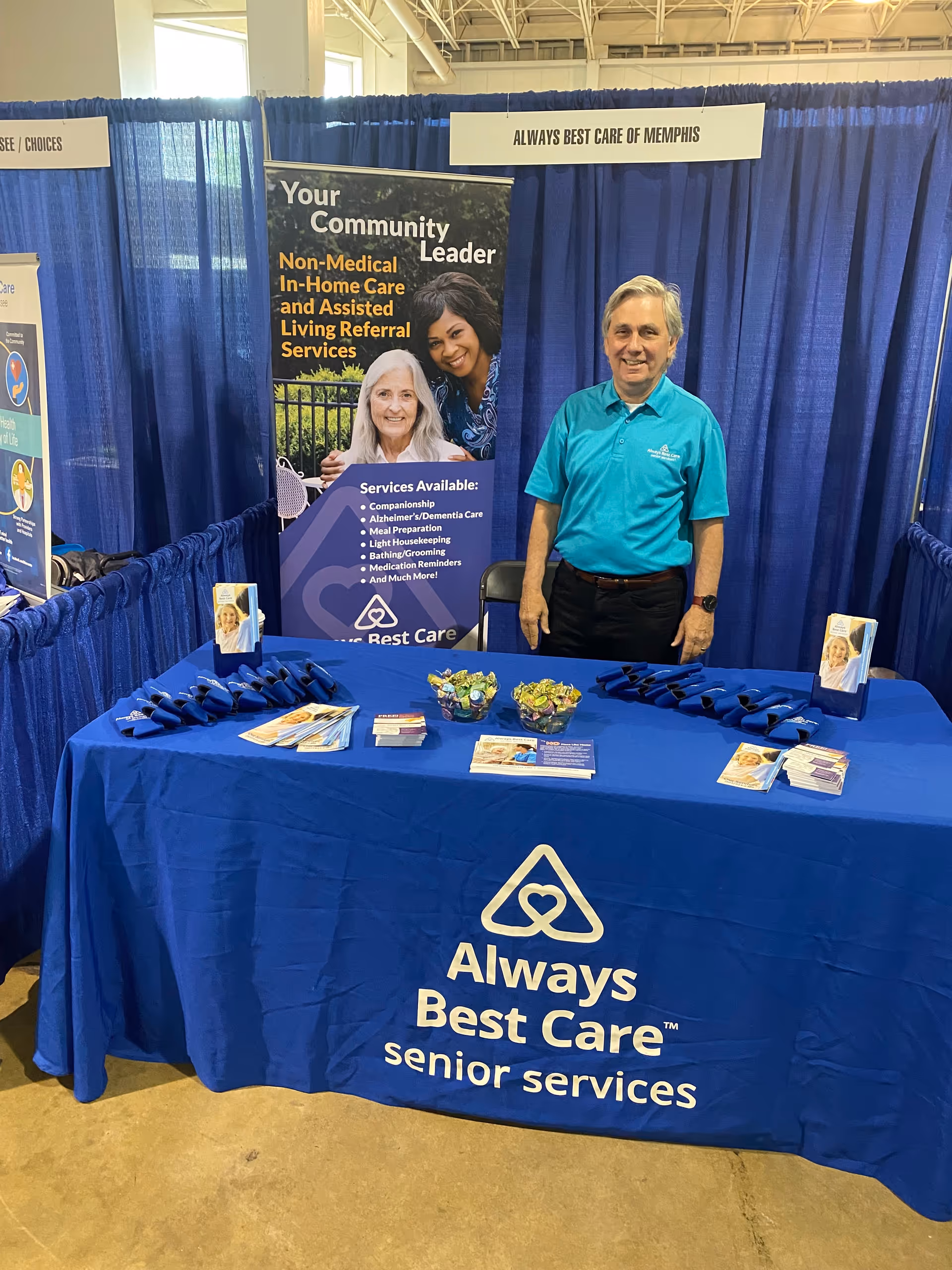 Man in turquoise polo at a blue Always Best Care booth at a senior services expo.