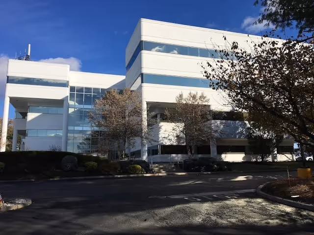 Modern white multi-story building with glass windows and a parking lot in front