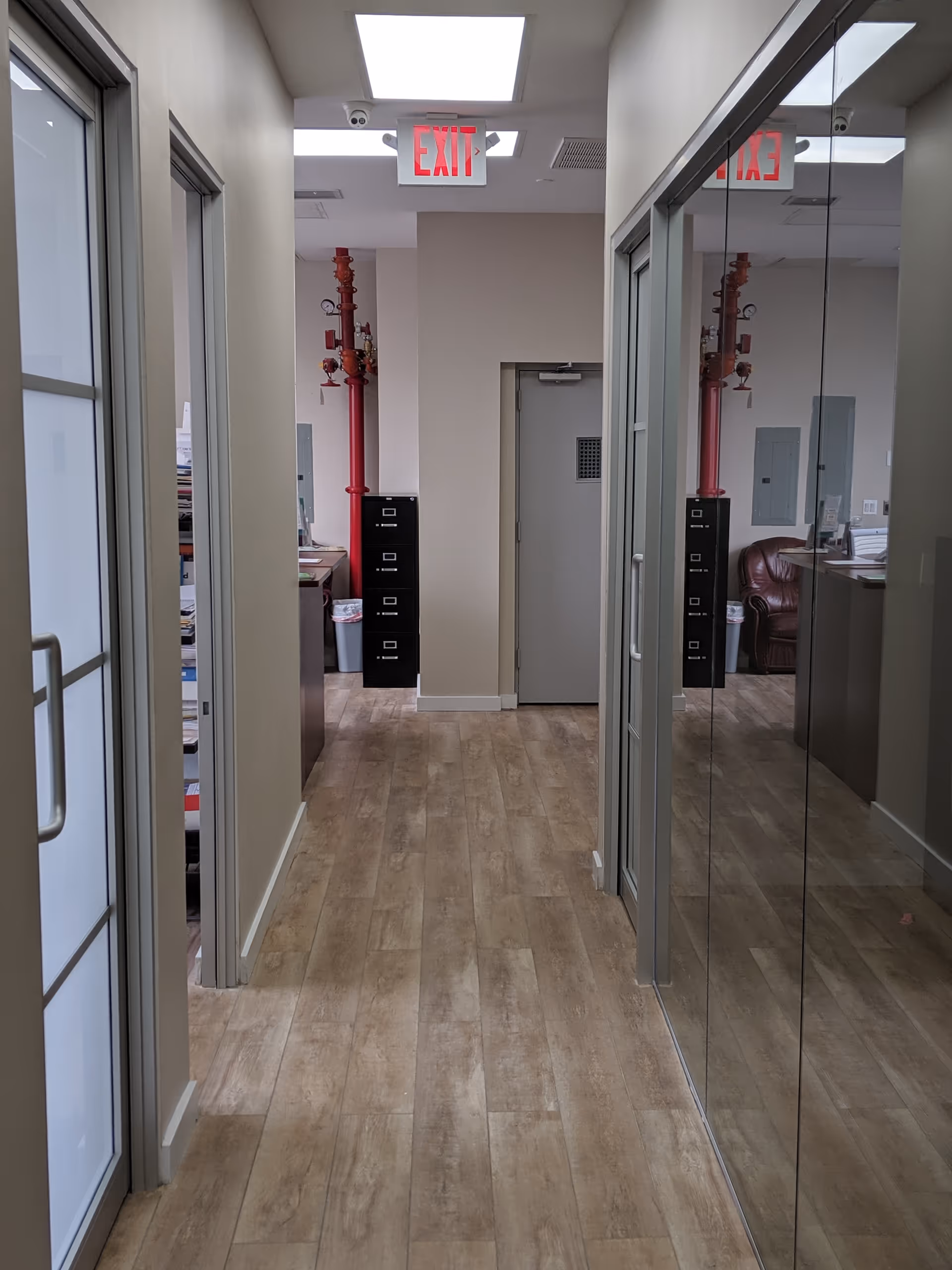 Interior corridor in a senior living facility with glass partitions, cabinets, and red pipes.