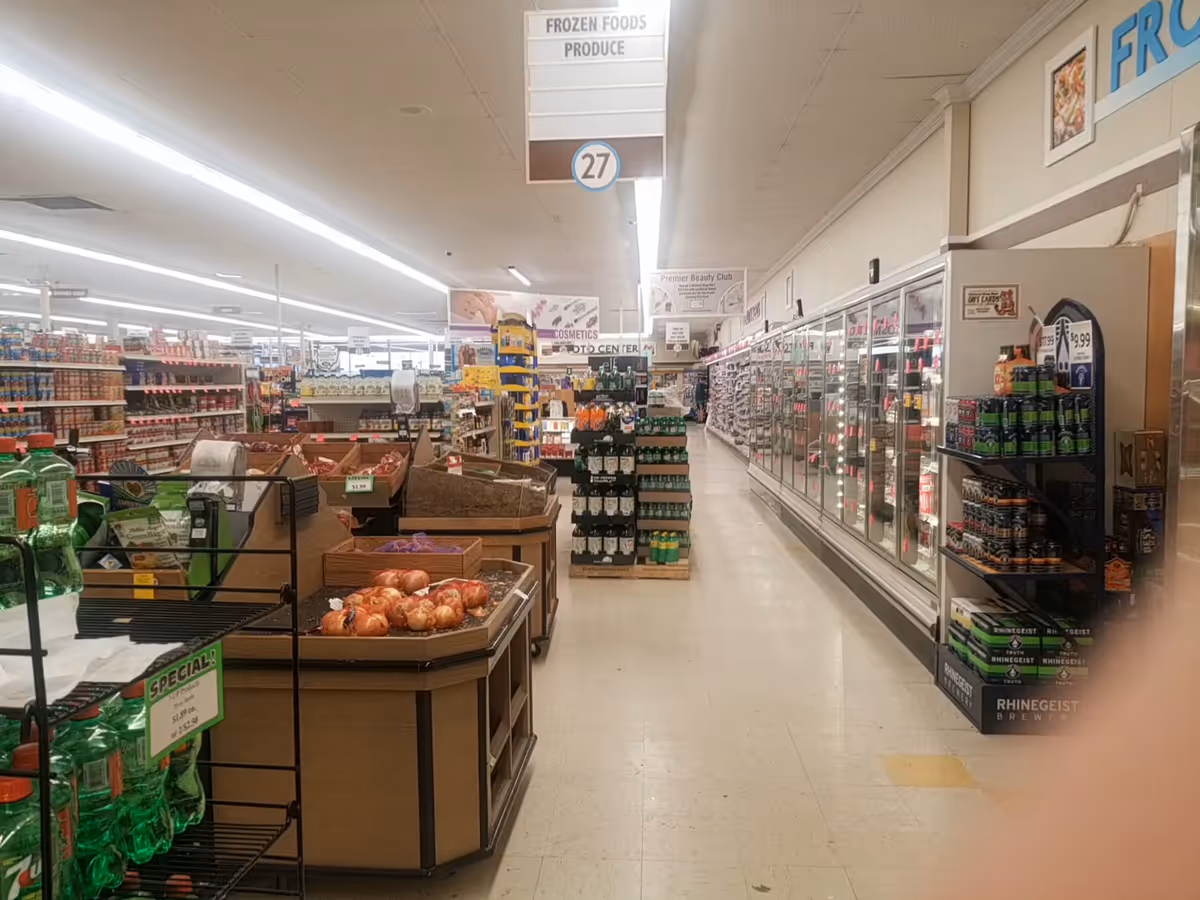 Grocery store interior with a long aisle, frozen food freezers, and displays.