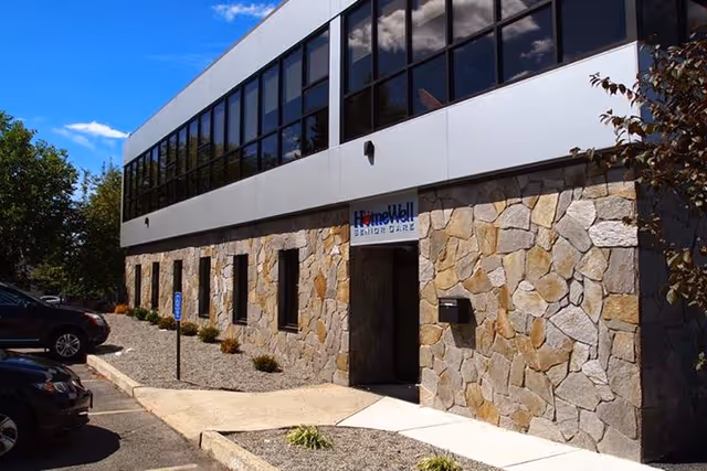 Exterior of a stone-clad building with HomeWell Senior Care sign and parking.
