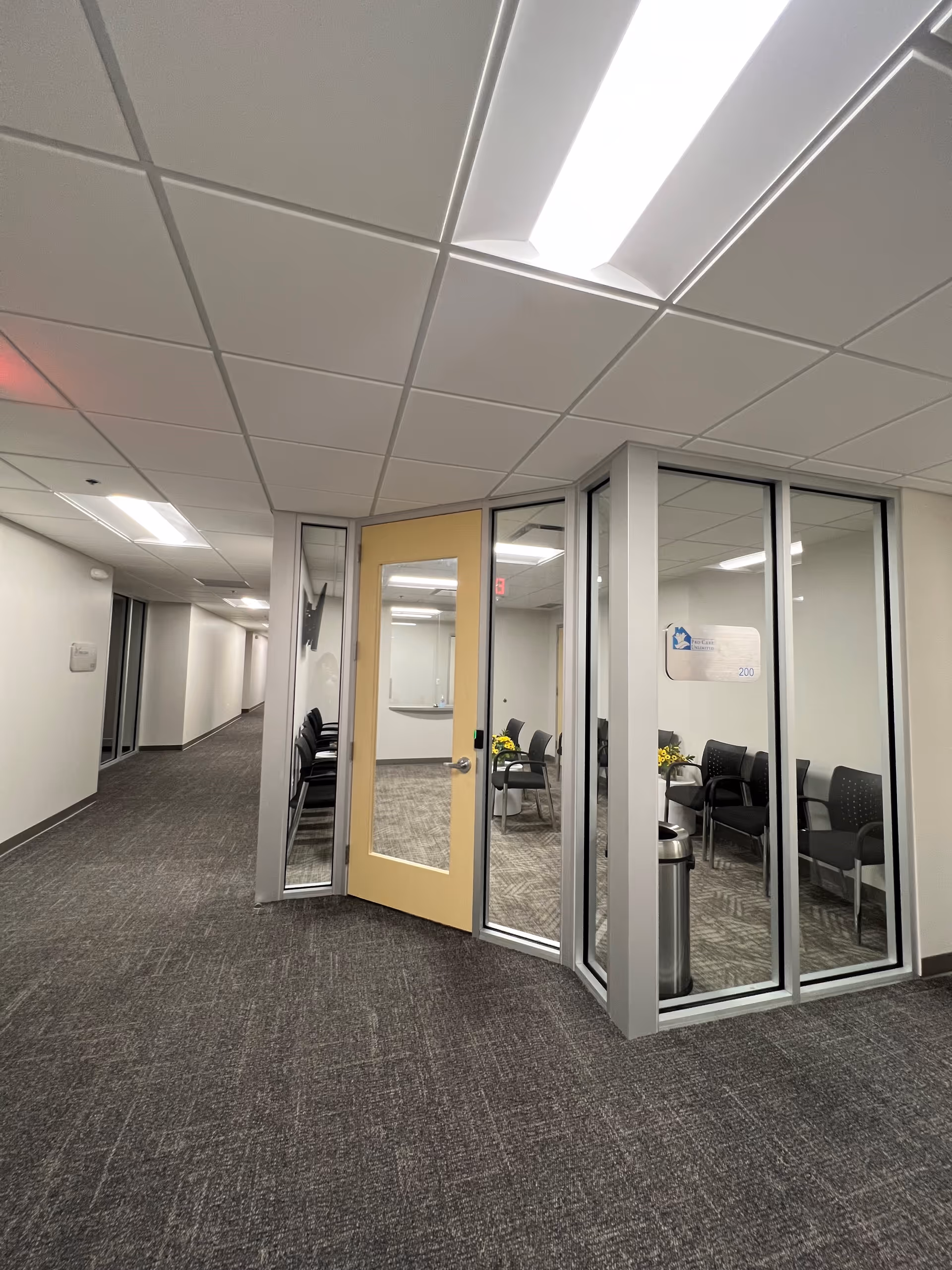 Interior corridor featuring glass-walled offices and a small reception area with chairs.