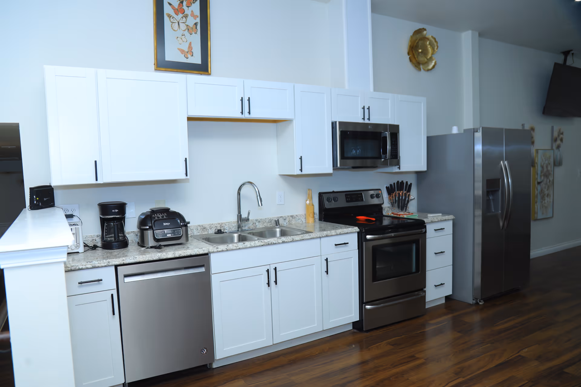 Modern white kitchen with stainless appliances, granite counters, and dark wood flooring.