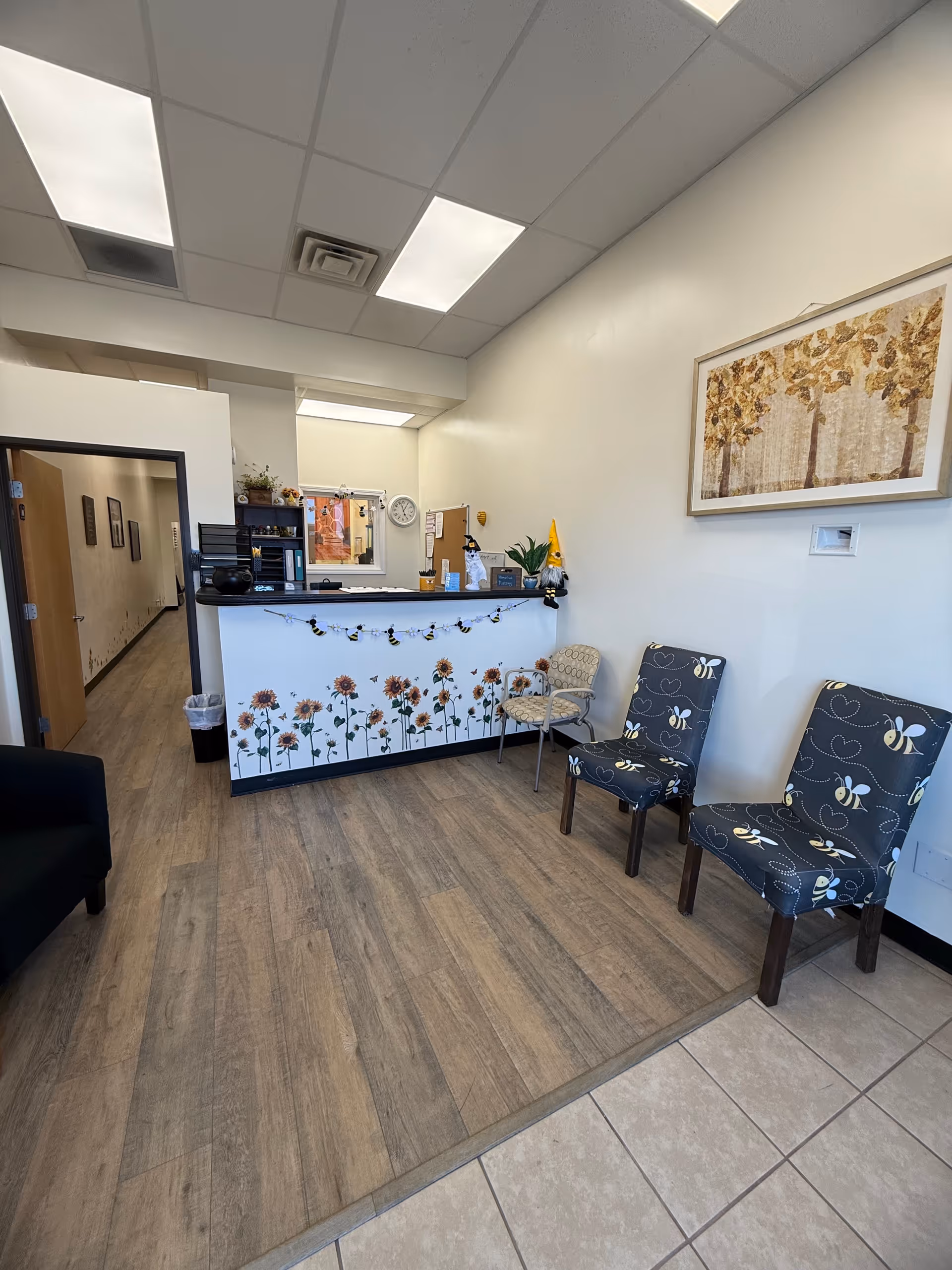 Reception area with sunflower-themed front desk, chairs, and hallway in a senior living facility.