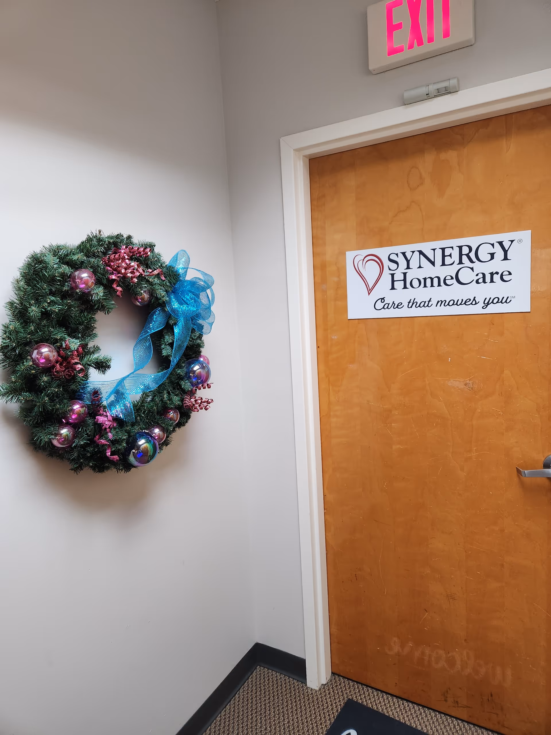 Interior hallway with a SYNERGY HomeCare door and festive wreath on wall.
