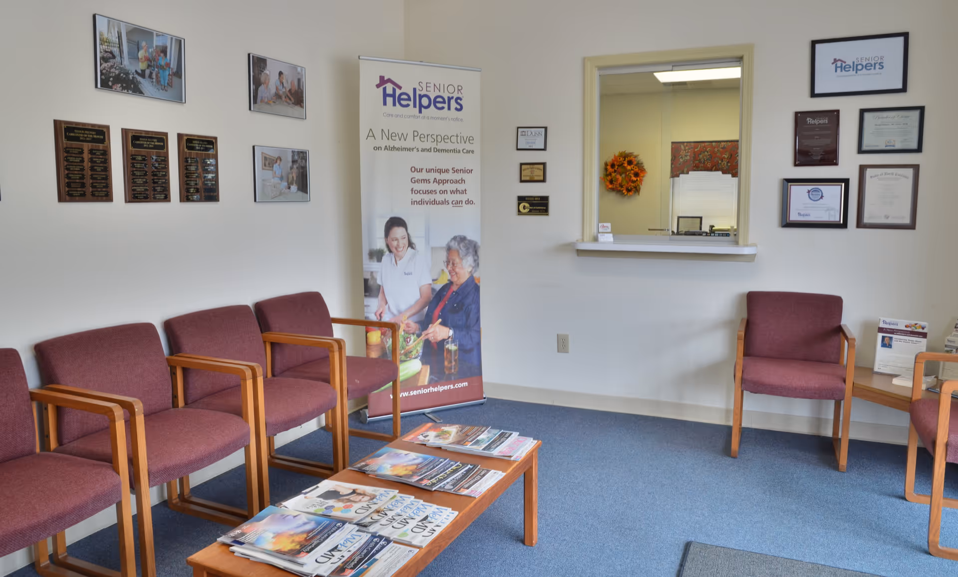 Waiting area in a Senior Helpers facility with maroon chairs and a reception window.
