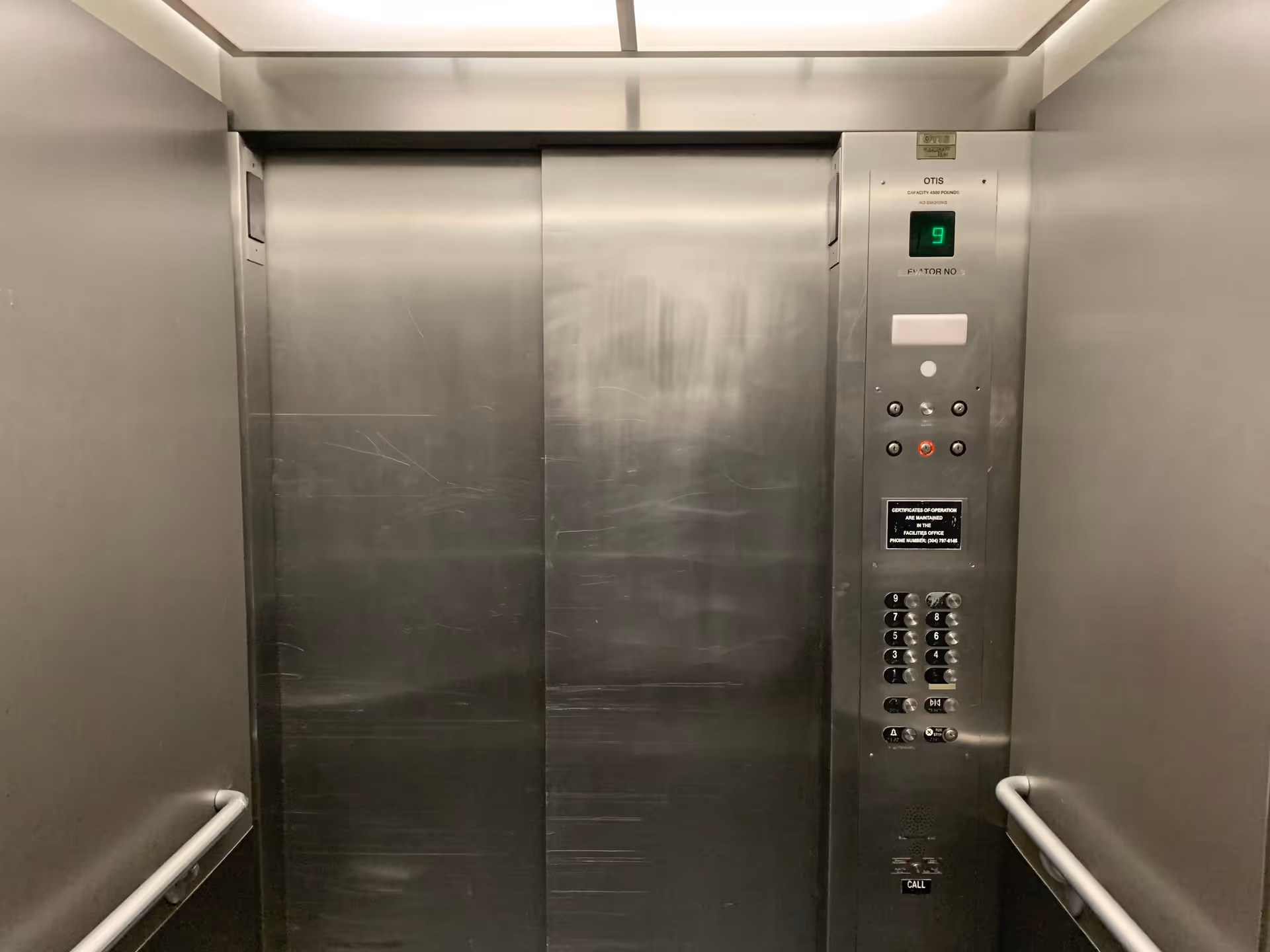 Metal elevator interior with control panel and closed stainless steel doors.