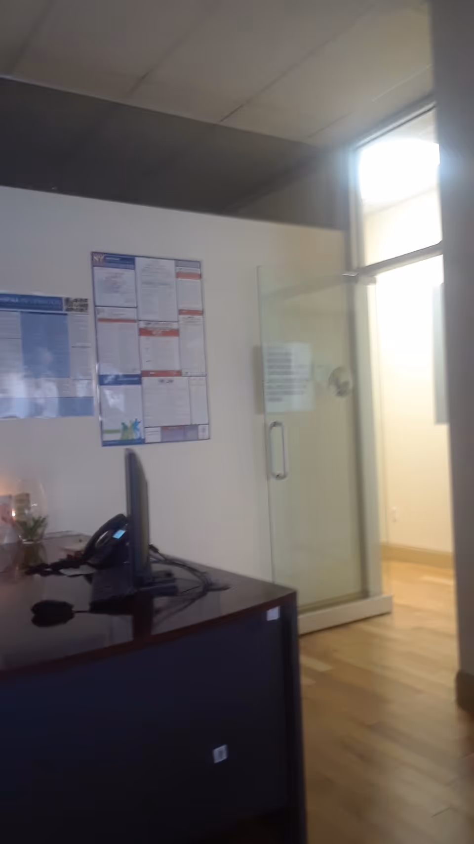 Reception desk with computer and wall posters beside a glass door in an office area.