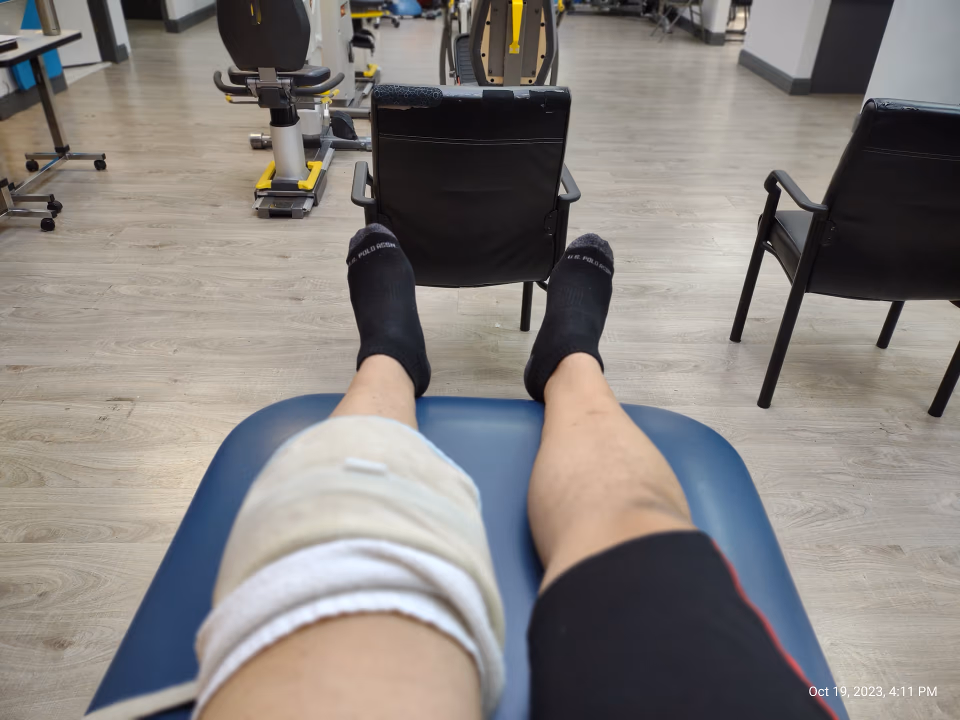 Patient’s legs with knee wrap rest on a chair in a JAG Physical Therapy room.