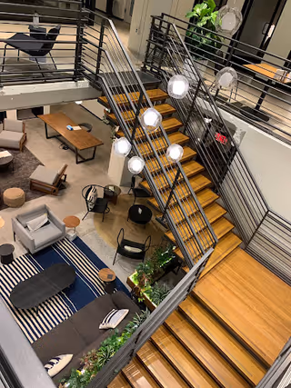 Multi-level senior living common area featuring a wooden staircase, lounge seating, and plants.