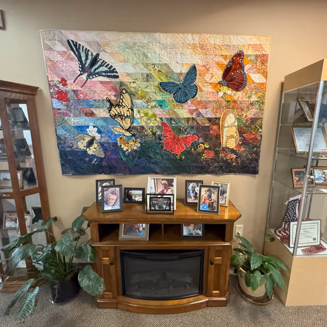 Lobby area with butterfly mural, wooden fireplace console, framed photos, and potted plants.