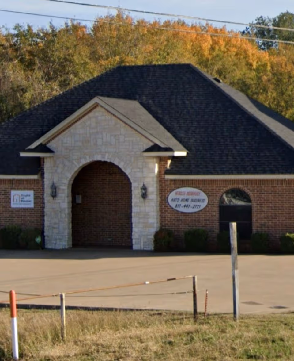 Exterior brick building with arched stone entrance and sign, front view of senior living facility.