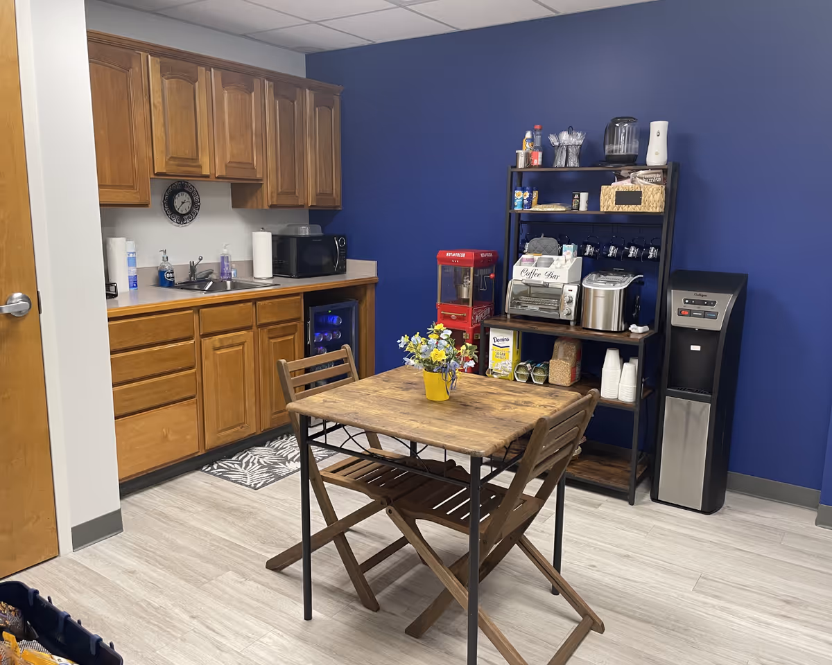 Wooden kitchenette area with dining table, chairs, blue wall, and coffee station.