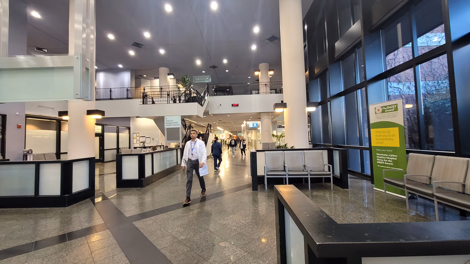 Bright Johns Hopkins Outpatient Center lobby with seating, reception desks, pillars, and people walking.