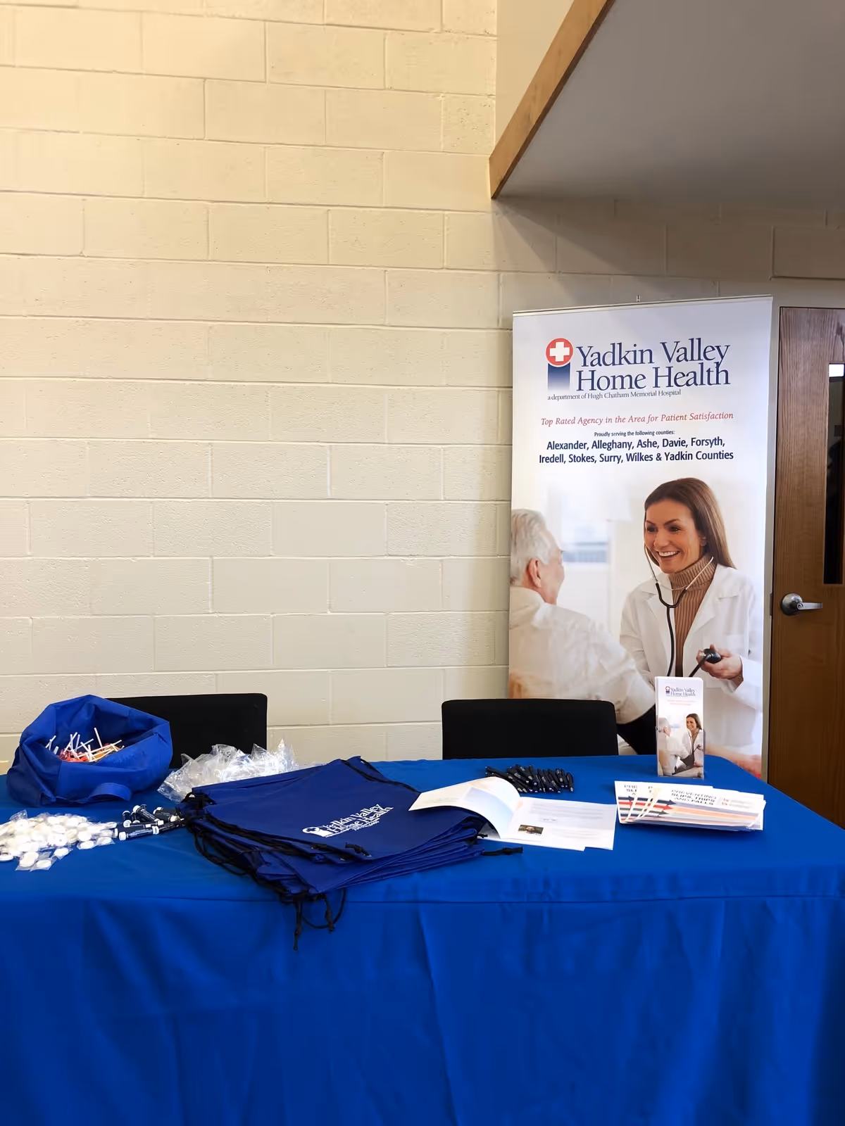 A blue-clothed promotional table with brochures and a Yadkin Valley Home Health banner indoors.