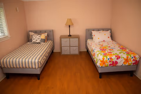 Two single beds with a nightstand and lamp between them in a peach bedroom.