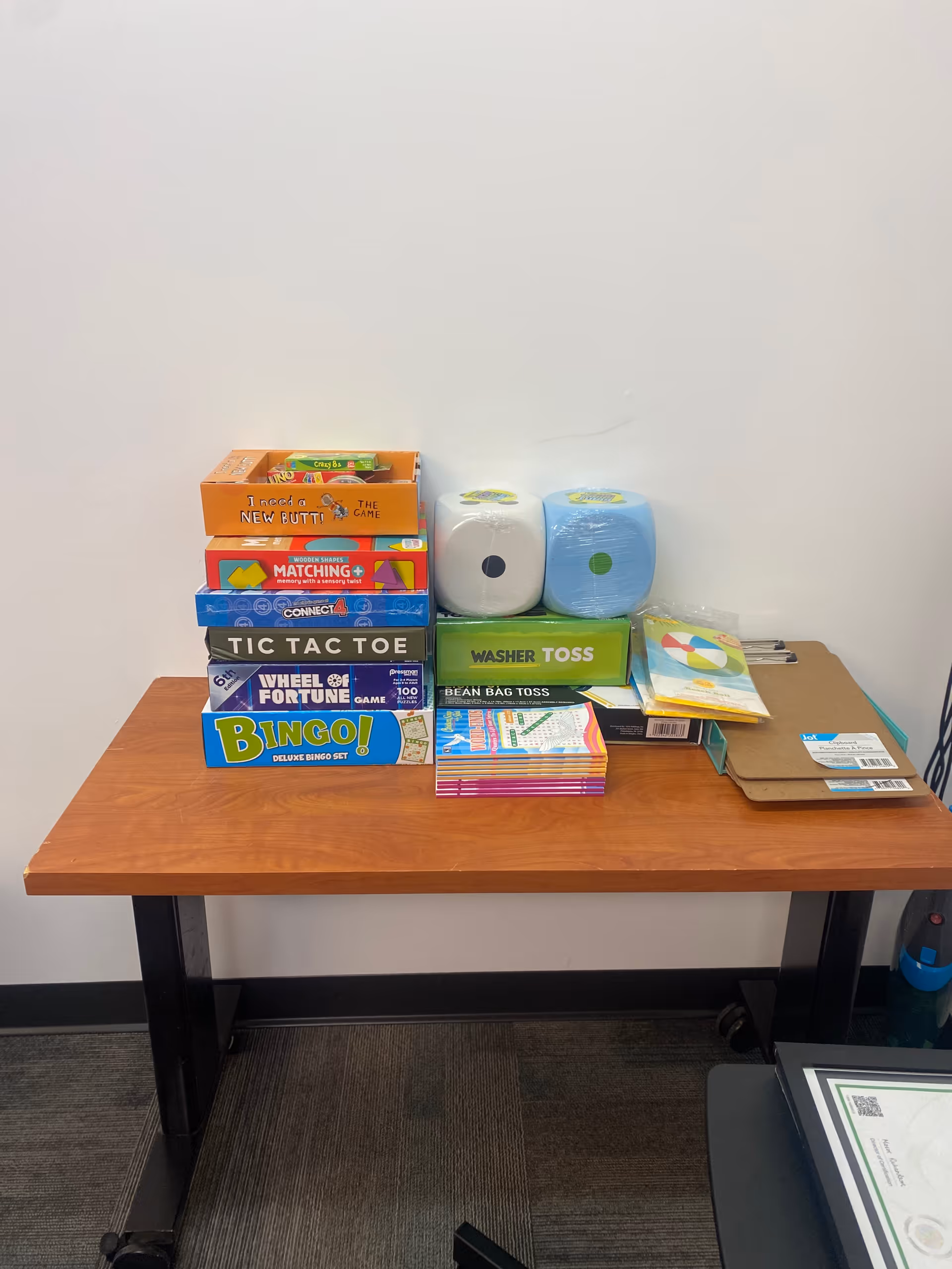 Table with assorted board games and supplies in a plain interior room.