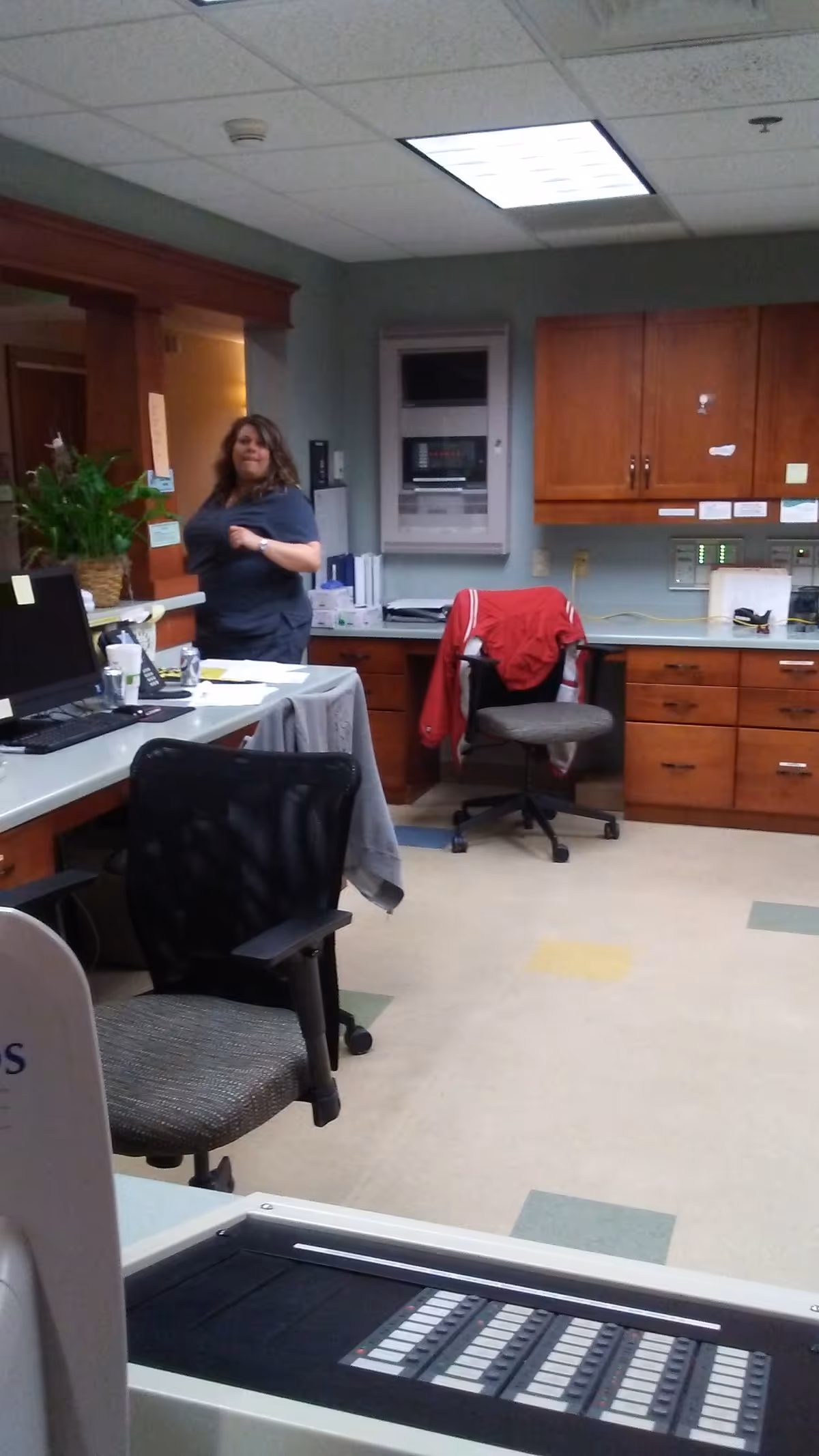 A staff member stands by a desk in a medical office area with cabinets and equipment.