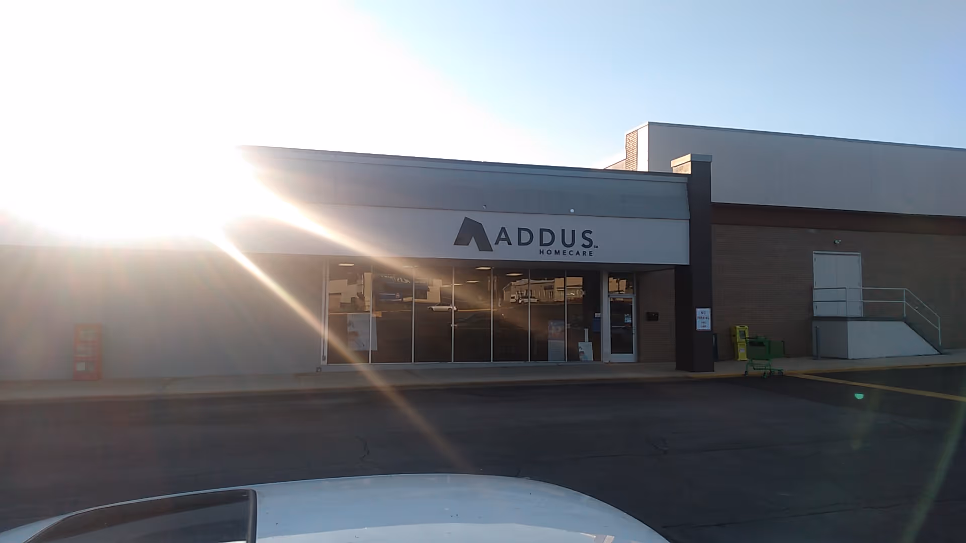 Exterior view of Addus HomeCare storefront with glass doors and bright sun glare.
